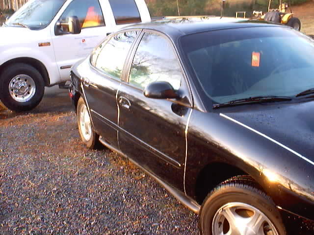 black sedan parked next to a white truck on a gravel lot