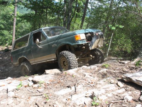 1978 Ford Bronco - Modified green Ford Bronco navigating a challenging rocky trail with its front end showing damage.
