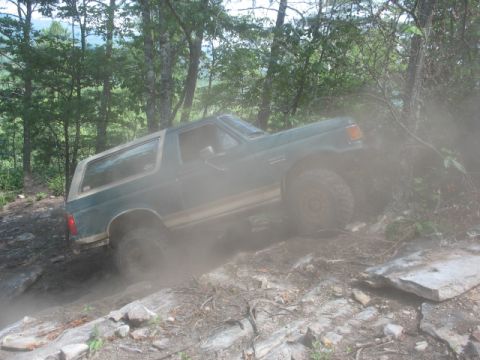 1978 Ford Bronco - A green Ford Bronco navigates a dusty, rocky trail through a wooded area.