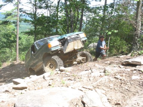 1978 Ford Bronco - A man attempts to push a green off-road SUV as it navigates a steep, rocky trail.