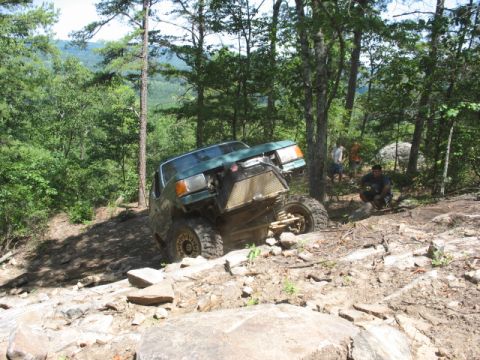 1978 Ford Bronco - Off-road vehicle navigating a challenging rocky incline in a wooded area.