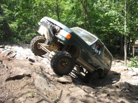 1978 Ford Bronco - Green SUV with lifted suspension navigates a rocky incline off-road.