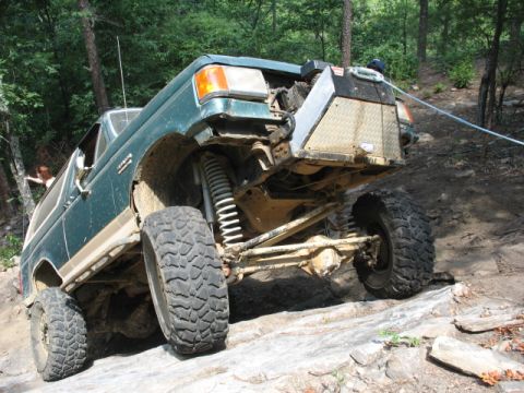 1978 Ford Bronco - This modified SUV is navigating a challenging rocky terrain with its front wheels high off the ground.