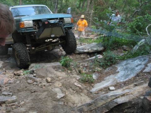 1978 Ford Bronco - Modified off-road vehicle tackling a challenging rocky path in a wooded area.