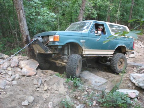 1978 Ford Bronco - A teal Ford Bronco navigates a challenging off-road course, its winch engaged to assist with traction on the rocky terrain.