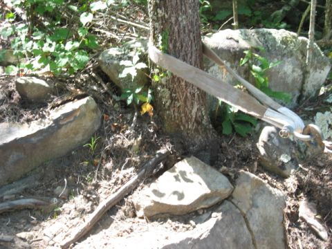 1978 Ford Bronco - A tree is secured by a strap and hook in a rocky, wooded area.