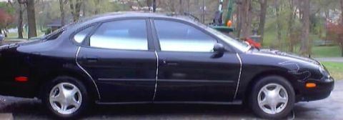 1999 Ford Taurus - Side profile of a black 1999 Ford Taurus sedan parked outdoors.