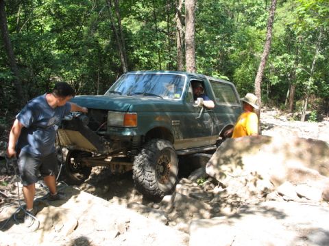 1978 Ford Bronco - A green SUV navigates a challenging rocky trail with two people assisting and observing.