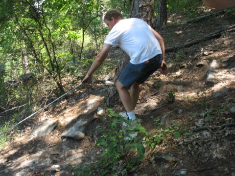 1978 Ford Bronco - A man grips a metal pole while navigating a steep, wooded incline.