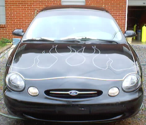 1999 Ford Taurus - A black 1999 Ford Taurus is shown from the front, white flame decals on its hood.