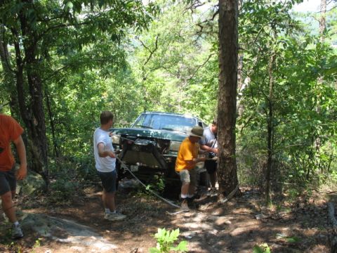 1978 Ford Bronco - Several people are working to winch a green off-road vehicle out of a wooded area.