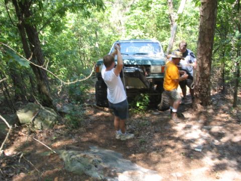 1978 Ford Bronco - People are using a winch to pull a green SUV out of a wooded area.