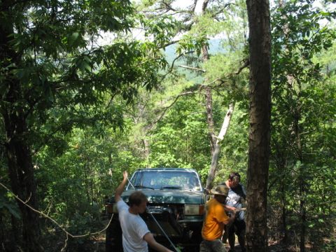1978 Ford Bronco - People working with a winch on a green SUV in a wooded area.