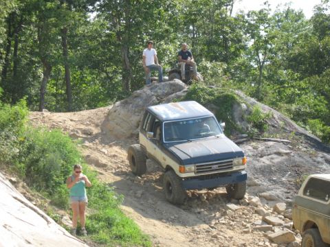 1978 Ford Bronco - Off-road vehicles navigate a challenging rocky trail with trees and people watching.