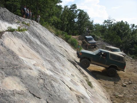 1978 Ford Bronco - A green 1978 Ford Bronco navigates a challenging rocky incline, with other off-road vehicles and spectators present.