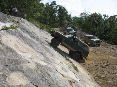 1978 Ford Bronco - Multiple off-road vehicles navigate a challenging rocky incline, with a green 1978 Ford Bronco prominently ascending the steep terrain.