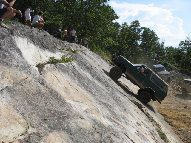 Green 1978 Ford Bronco climbing a steep rock face with spectators watching from above