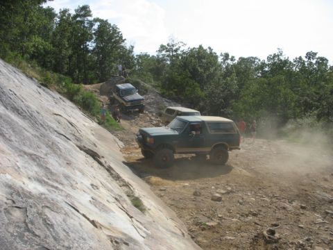 1978 Ford Bronco - Several off-road vehicles navigate a challenging dirt and rock trail under a partly cloudy sky.