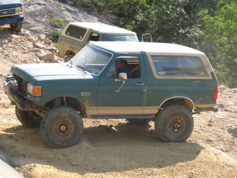1978 Ford Bronco - A modified green Ford Bronco navigates a challenging off-road terrain with other vehicles present.