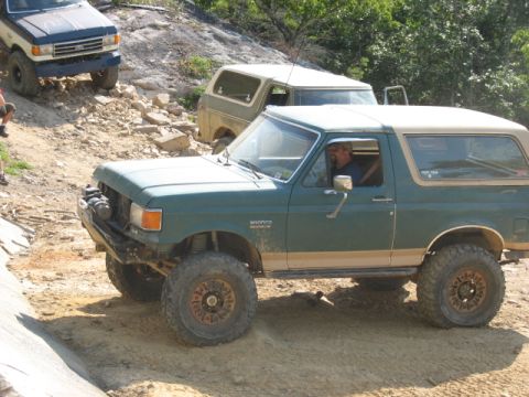 1978 Ford Bronco - A green Ford Bronco navigates a rocky off-road trail with other vehicles visible.