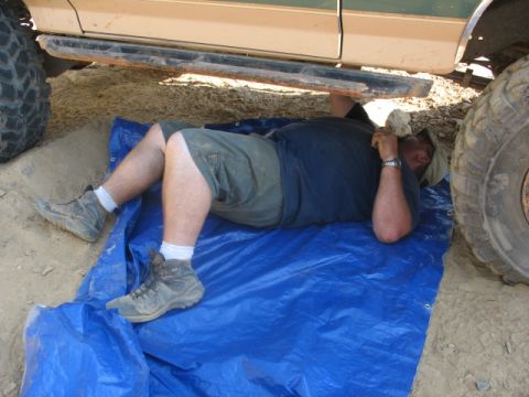 1978 Ford Bronco - A person works on the underside of a large SUV, lying on a blue tarp.
