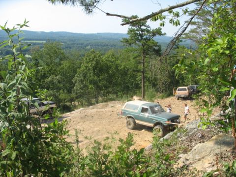 1978 Ford Bronco - Several off-road vehicles navigate a challenging dirt path on a hillside with a distant view of rolling hills.