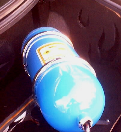 1999 Ford Taurus - Close-up of a blue canister with a yellow label, possibly a fluid reservoir, located in the trunk of a vehicle.
