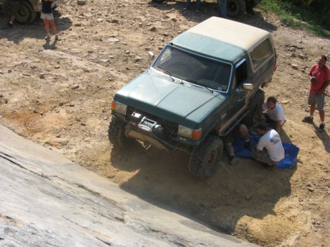 1978 Ford Bronco - A group of people are working on a lifted Ford Bronco on a dirt trail, with another vehicle visible in the background.