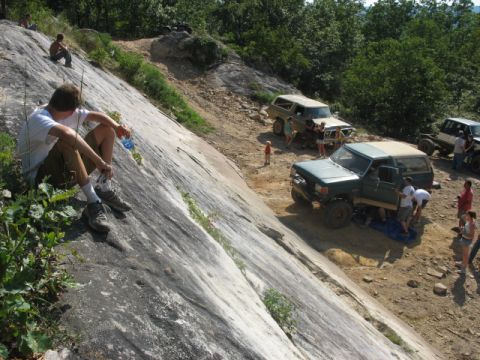 1978 Ford Bronco - Several off-road vehicles are parked on a dirt trail next to a steep, rocky slope where people are gathered.