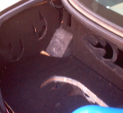 Inside of a car trunk, showing the dark carpet lining and some plastic trim pieces