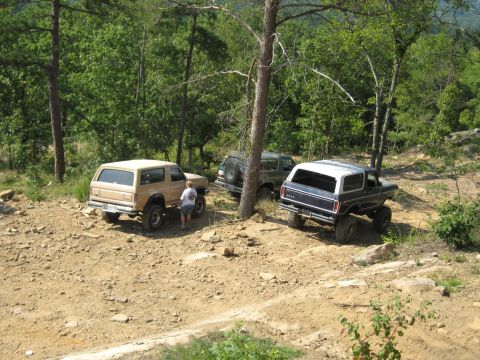 1978 Ford Bronco - Three Ford Broncos navigate a off-road trail surrounded by trees.