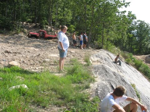 1978 Ford Bronco - A red pickup truck is stuck in a dirt area with people standing around.