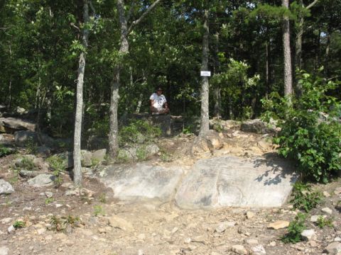 1978 Ford Bronco - A person sits in a meditative pose on a large rock surrounded by trees and rocky terrain.