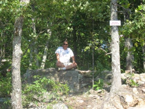 1978 Ford Bronco - Man meditating on a rock in a forest clearing. A sign is visible on a nearby tree.