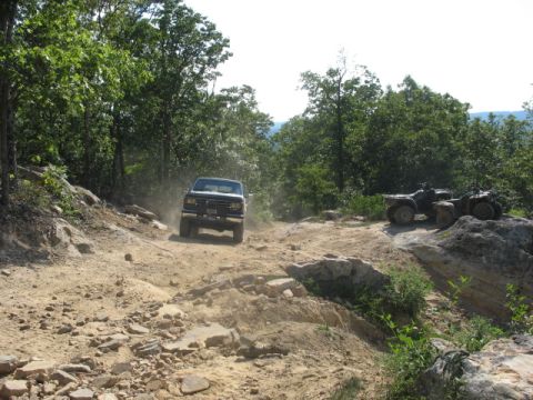 1978 Ford Bronco - A truck navigates a challenging off-road path while ATVs rest nearby.