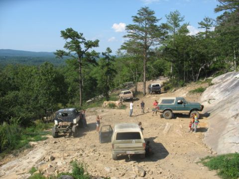 1978 Ford Bronco - Several off-road vehicles navigate a steep, rocky trail under a clear blue sky.
