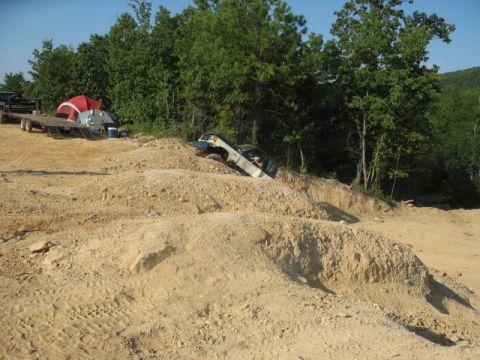 1978 Ford Bronco - A white off-road vehicle navigates a steep dirt incline with a trailer and tents in the background.