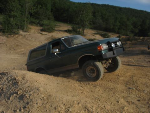 1978 Ford Bronco - This green SUV is shown off-roading on a dirt track, with its front lights visible.