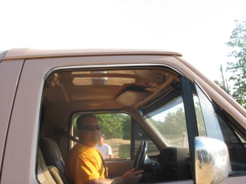 guy in orange shirt driving a light brown pickup truck, another person visible in background