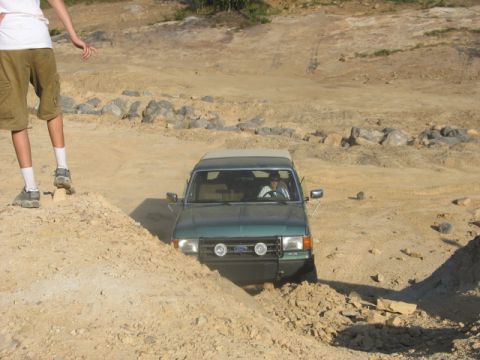 Green SUV with a brush guard and auxiliary lights driving through a dirt track. A person is visible in the dri