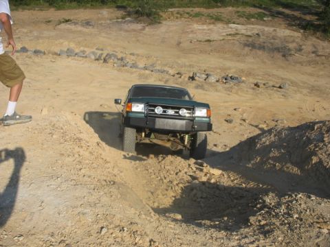 Green off-road truck with aftermarket bumper and auxiliary lights navigating a dirt track