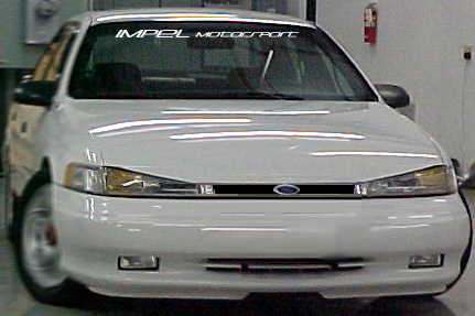 1993 Ford Taurus - Front view of a white 1993 Ford Taurus, an 'IMPEL MOTORSPORT' banner on the windshield.