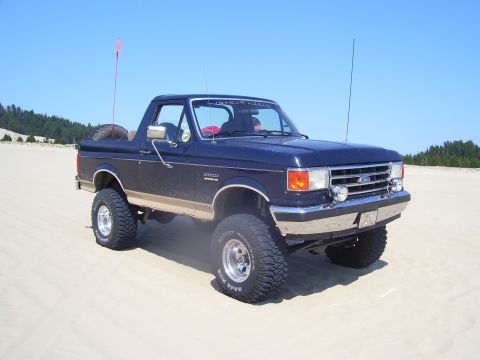 1991 Ford Bronco - This lifted 1991 Ford Bronco is shown on a sandy terrain under a clear blue sky.