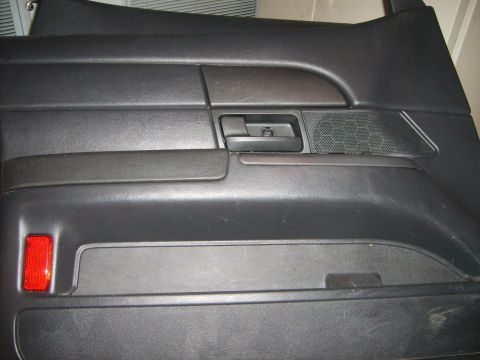 1993 Ford Crown Victoria - A black car door panel is shown, a red reflector and a hexagonal speaker grille.