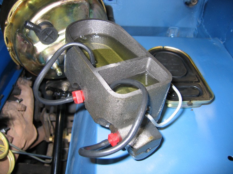 Close-up of a dual-chamber master cylinder with brake booster attached. Yellow fluid is visible in the reservoir