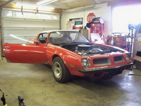 1974 Pontiac Firebird - A red 1974 Pontiac Firebird is parked in a garage with its hood open and driver's door ajar, suggesting it is undergoing restoration.