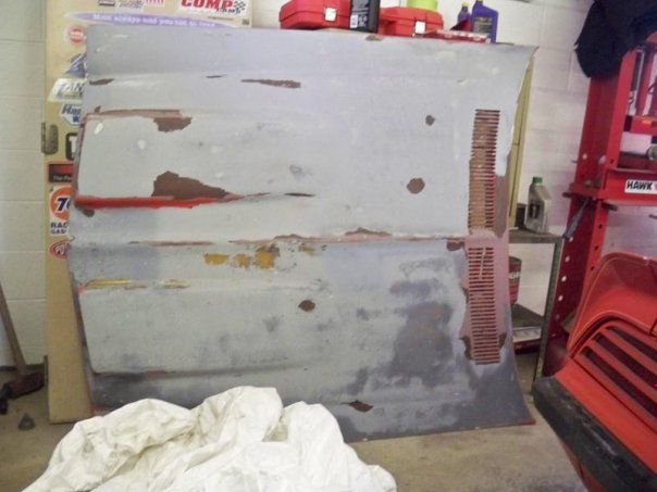 car hood with peeling paint and rust spots, sitting in a garage