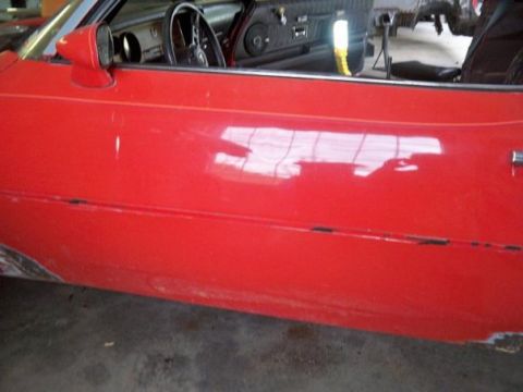 1974 Pontiac Firebird - Close-up of a red car's interior and door, showing signs of wear and tear.