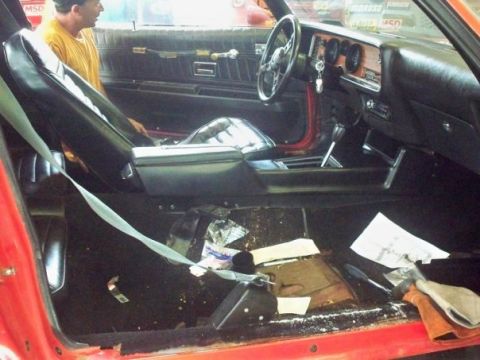 1974 Pontiac Firebird - The interior of a red car shows a messy floor with papers and debris scattered around.
