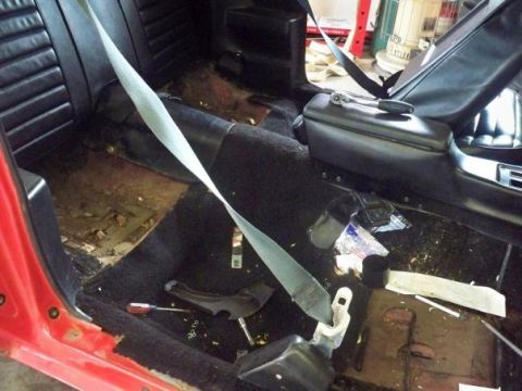 1974 Pontiac Firebird - The interior of a red car is shown, black seats and a seatbelt, with tools on the floor indicating ongoing work.